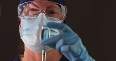 Doctor With Face Mask and latex gloves holding a botthe of vaccine and syringe, American flag reflected on protection glasses video