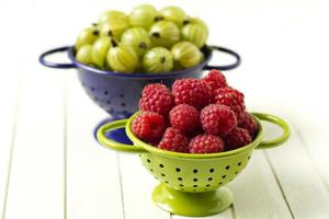 Fresh gooseberries and raspberries in colofrul colanders photo
