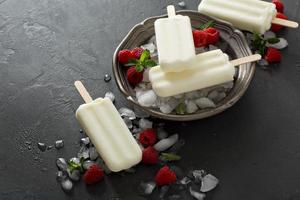 Coconut popsicles with raspberries on black background photo