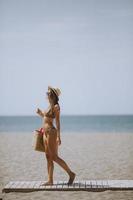 Young woman in bikini with straw bag on the beach at summer day photo