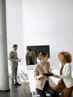 Young businesswomen discussing with digital tablet in the office with young people works behind them photo