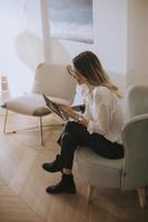 mujer morena sonriente sentada en una silla con tableta digital en un salón luminoso foto