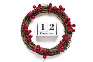 Christmas wreath decorated with red berries, wooden calendar date 12 December isolated on white background Concept of Christmas preparation, atmosphere Wishes card Hand made Christmas wreath Flat lay photo