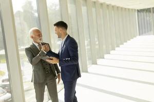 Mature businessman and his young colleague discussing finantial report on   digital tablet in the office corridor photo