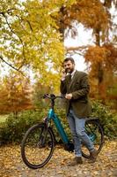 Joven con bicicleta eléctrica en el parque de otoño foto