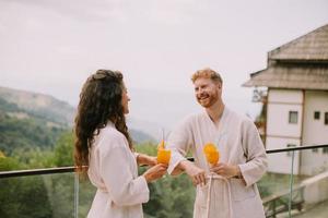 pareja joven relajándose en la terraza al aire libre y bebiendo jugo de naranja fresco foto