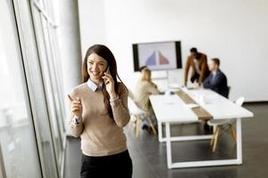 Young business woman standing in the office and using mobile phone in front of her team photo