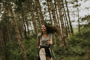 Young woman taking a walk with trekking poles in the forest, carrying a backpack photo