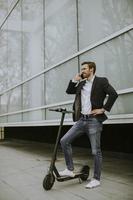 Young businessman using mobile phone  on electric scooter photo