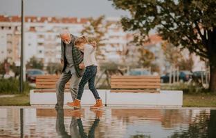 Grandfather spending time with his granddaughter by small water pool in park on autumn day photo