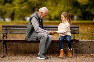 Grandfather playing red hands slapping game with his granddaughter in park on autumn day photo