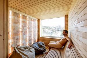 Young man relaxing in the sauna and watching winter forest through the window photo