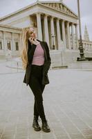 bella mujer sonriente usando teléfono móvil y caminando por el parlamento austríaco en viena, austria foto