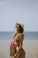 Young woman in bikini with straw bag on the beach at summer day photo