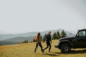 Smiling couple walking with backpacks over green hills photo