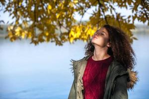 Curly hair teen girl standing by river photo