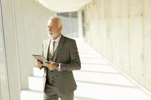 Mature businessman standing with digital tablet in the office corridor photo