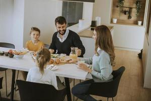 Young happy family talking while having breakfast at dining table photo