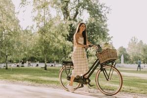 mujer joven con bicicleta eléctrica y flores en la cesta foto