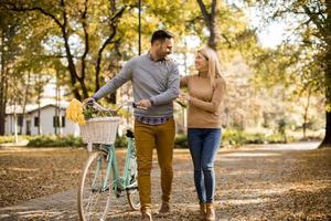 Active senior couple together enjoying romantic walk with bicycle in golden autumn park