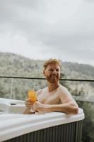 Young man enjoying in outdoor hot tub and drink fresh orange juice on vacation photo