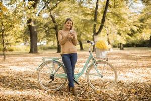 mujer joven, con, bicicleta, utilizar, smartphone, en, otoño, parque