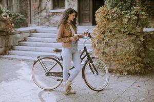 Young woman with mobile phone drink coffee to go by the bicycle on autumn day photo