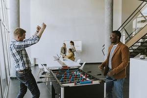 jóvenes empresarios multiétnicos casuales jugando futbolín y relajándose en la oficina foto