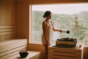 Young woman pouring water onto hot stone in the sauna photo