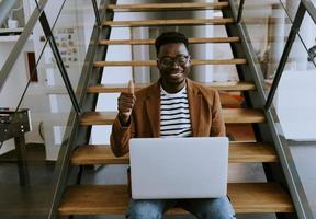 Young African American business man working on laptop computer while sitting on a office stairs photo