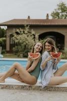 Young women sitting by the swimming pool and eating watermelon in the house backyard photo