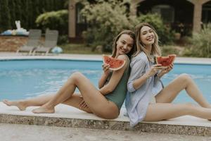 Young women sitting by the swimming pool and eating watermellon in the house backyard photo