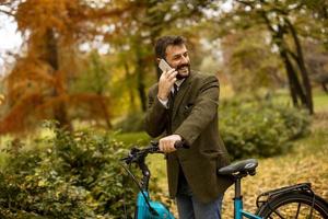 Young man with electric bicycle in the autumn park photo