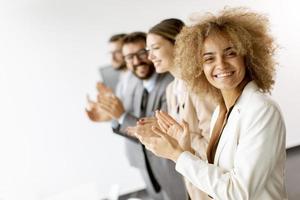 Group of diverse young coworkers standing in a row and applauding at office photo