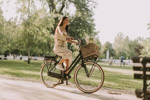 mujer joven montando bicicleta eléctrica con flores en la cesta foto
