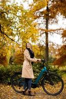 mujer joven con bicicleta eléctrica en el parque de otoño foto