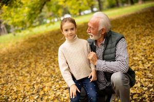 Grandfather spending time with his granddaughter in park on autumn day photo