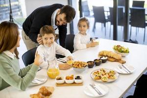 Young happy family talking while having breakfast at dining table photo