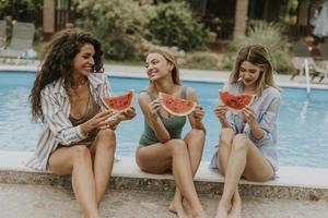 Young woman sitting on by the swimming pool and eating watermelon in the house backyard photo