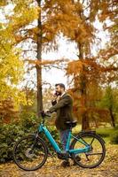 Young man with electric bicycle in the autumn park photo