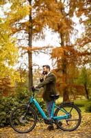 Joven con bicicleta eléctrica en el parque de otoño foto