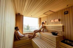 pareja joven relajándose en la sauna y viendo el bosque de invierno a través de la ventana foto