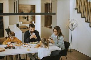 familia usando teléfonos móviles mientras desayuna en la mesa del comedor en el apartamento foto