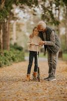 Senior man teaching his granddaughter how to ride kick scooter in park photo