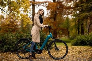 mujer joven con bicicleta eléctrica en el parque de otoño