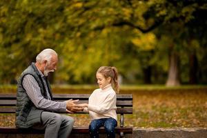 Grandfather playing red hands slapping game with his granddaughter in park on autumn day photo