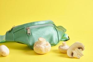 green belt bag made of eco leather and champignons on a yellow background, vegan leather concept photo