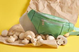 green belt bag made of eco leather and champignons on a yellow background, vegan leather concept photo