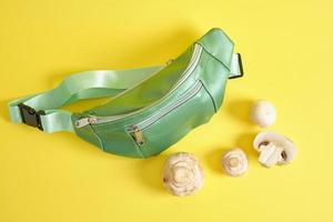 green belt bag made of eco leather and champignons on a yellow background, vegan leather concept photo