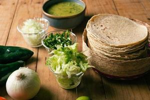 tortillas, bol con salsa verde y verduras sobre una mesa de madera. comida típica mexicana. foto